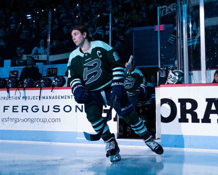 Knight skates out of the open bench door, looking to her right as she heads that way. She is wearing a green home uniform.