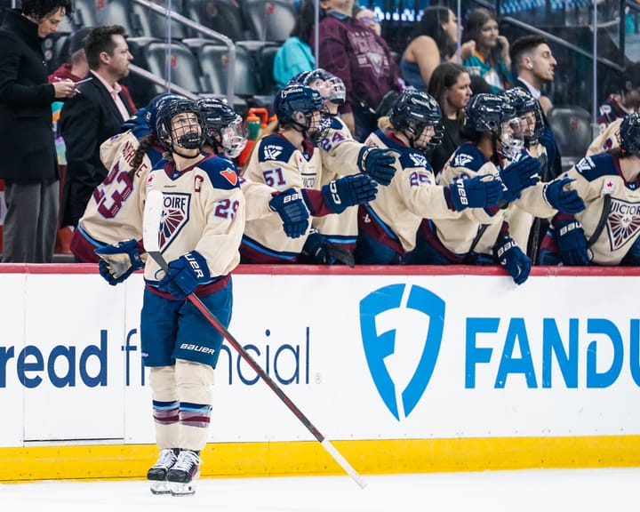 Poulin looks up at the scoreboard and smiles after going down the handshake line at the bench. She is wearing a cream away uniform.