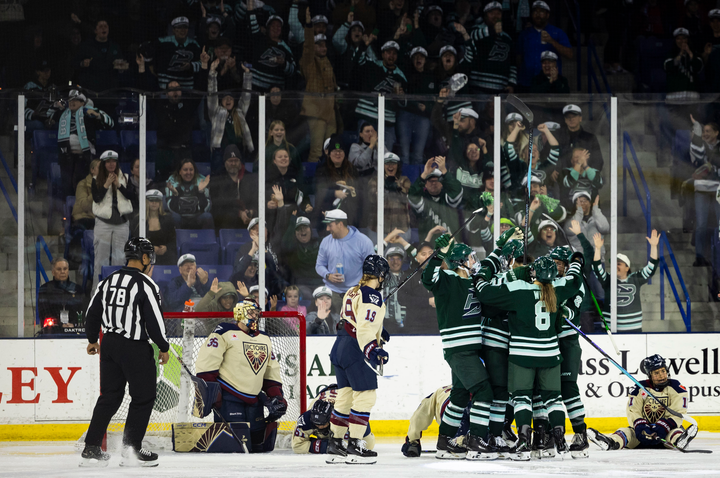 The Fleet celebrate with a group hug by the Montréal net. Cheering fans are in the background. The Fleet are wearing green home uniforms, while the Victoire are in cream away ones.