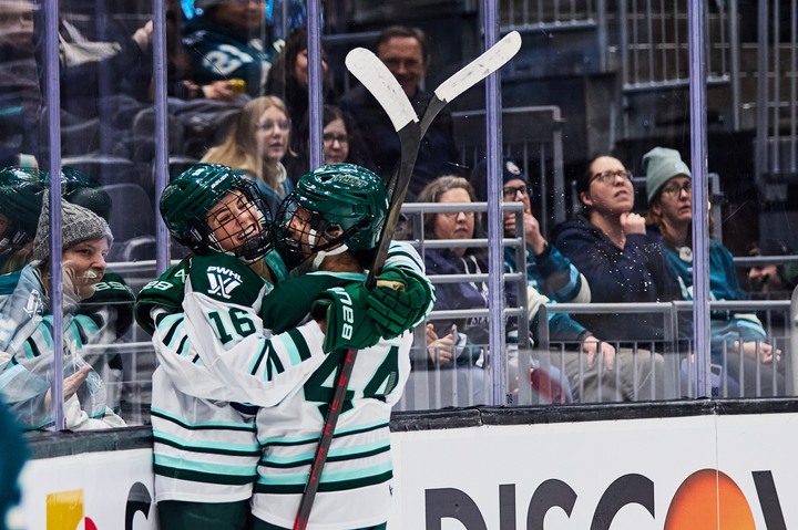 Brengman and Saulnier smile as they hug in the corner. They are both wearing white away uniforms.