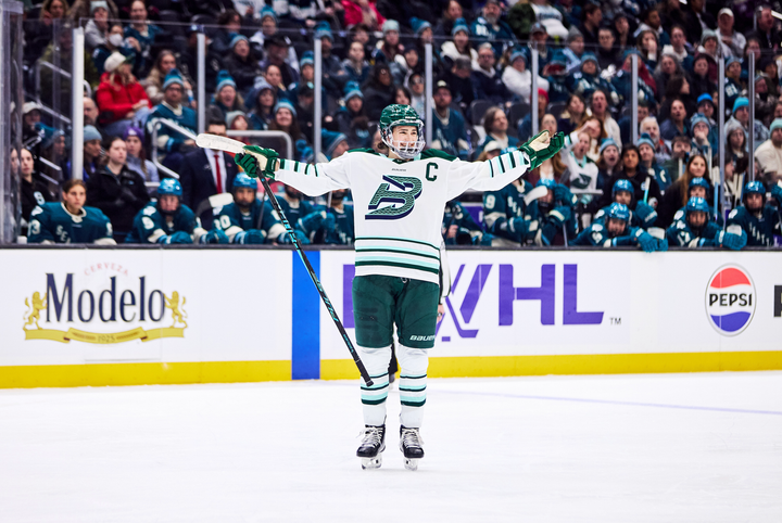 Keller smiles and opens her arms wide in celebration. She is wearing a white away uniform.